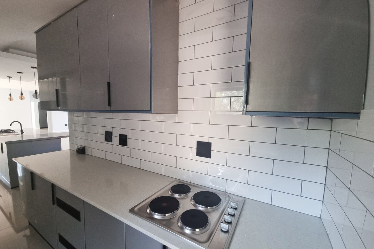 Modern kitchen featuring grey cabinetry, white subway tile backsplash, stone countertops, and a built-in electric hob.