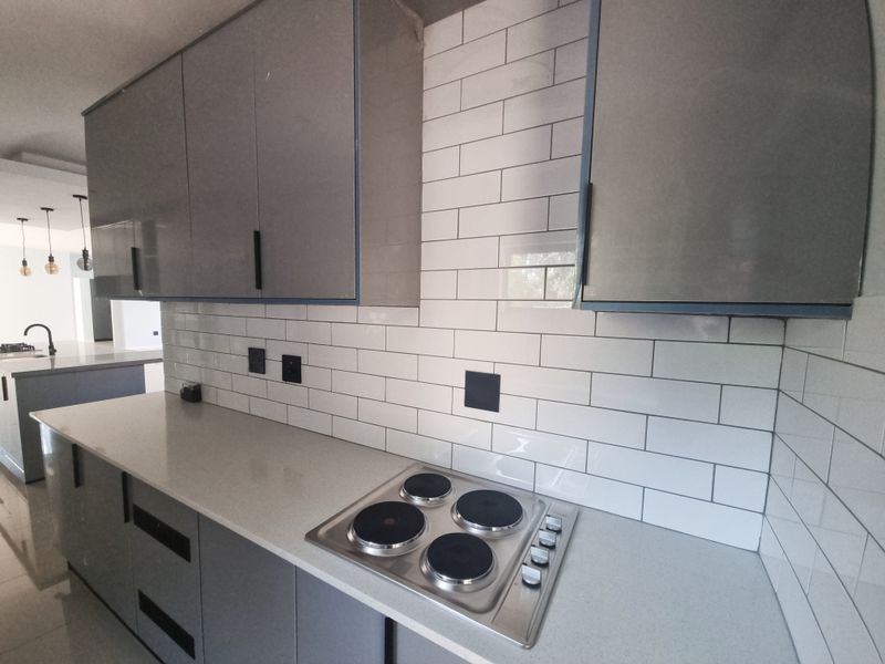 Modern kitchen featuring grey cabinetry, white subway tile backsplash, stone countertops, and a built-in electric hob.