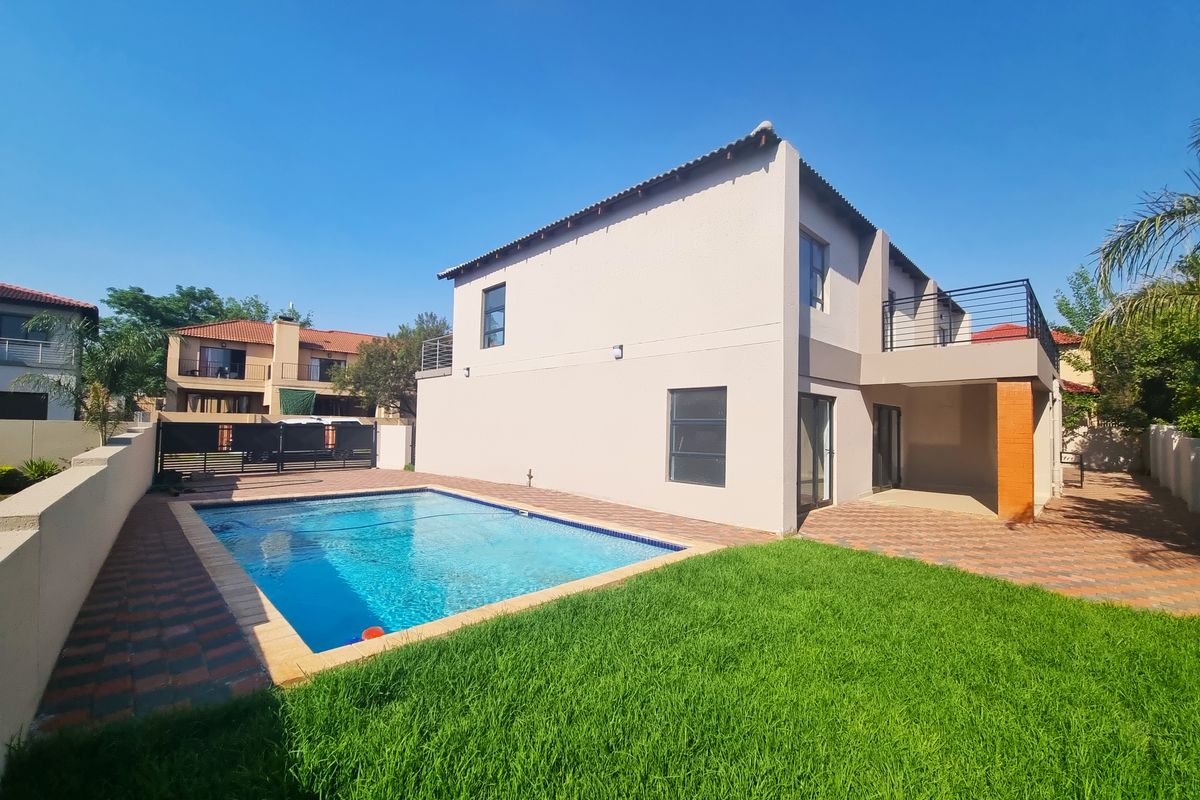 Rear view of the property featuring a swimming pool, paved patio area, and an upper-level balcony with metal railings.