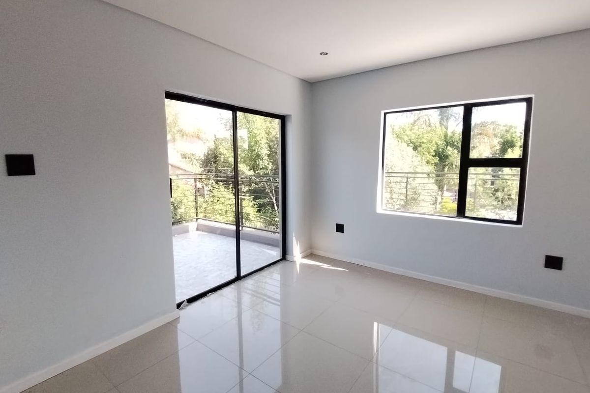 A bright, empty bedroom featuring modern tiled flooring, recessed lighting, and a sliding glass door providing access to a private balcony.