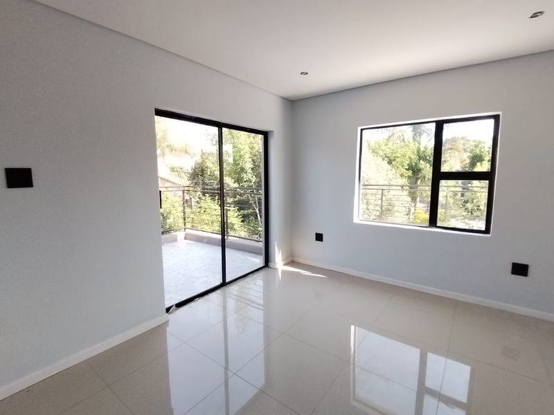 A bright, empty bedroom featuring modern tiled flooring, recessed lighting, and a sliding glass door providing access to a private balcony.