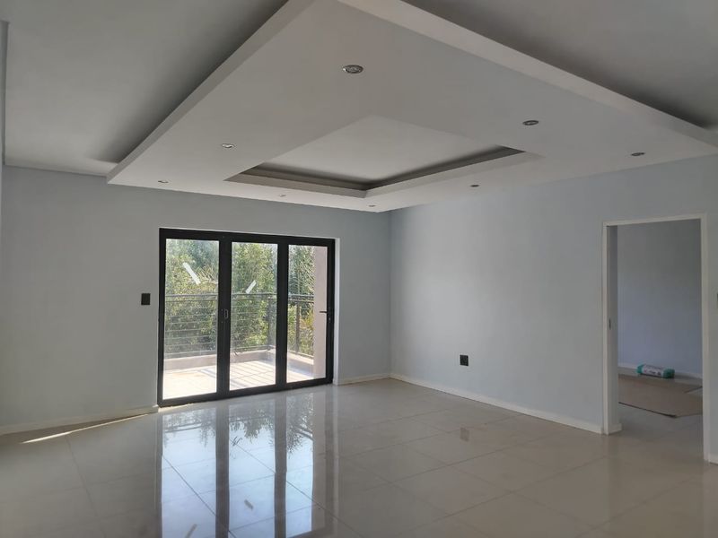 Spacious living area featuring modern recessed ceiling with downlights, polished tile flooring, and large aluminium sliding doors leading to an outdoor balcony.