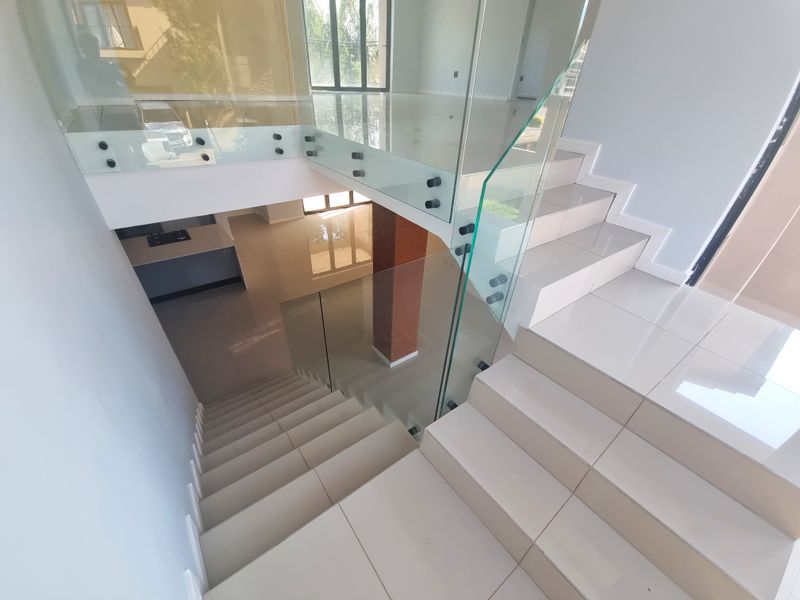 Modern staircase featuring a frameless glass balustrade with stainless steel fixings and high-gloss porcelain floor tiles.