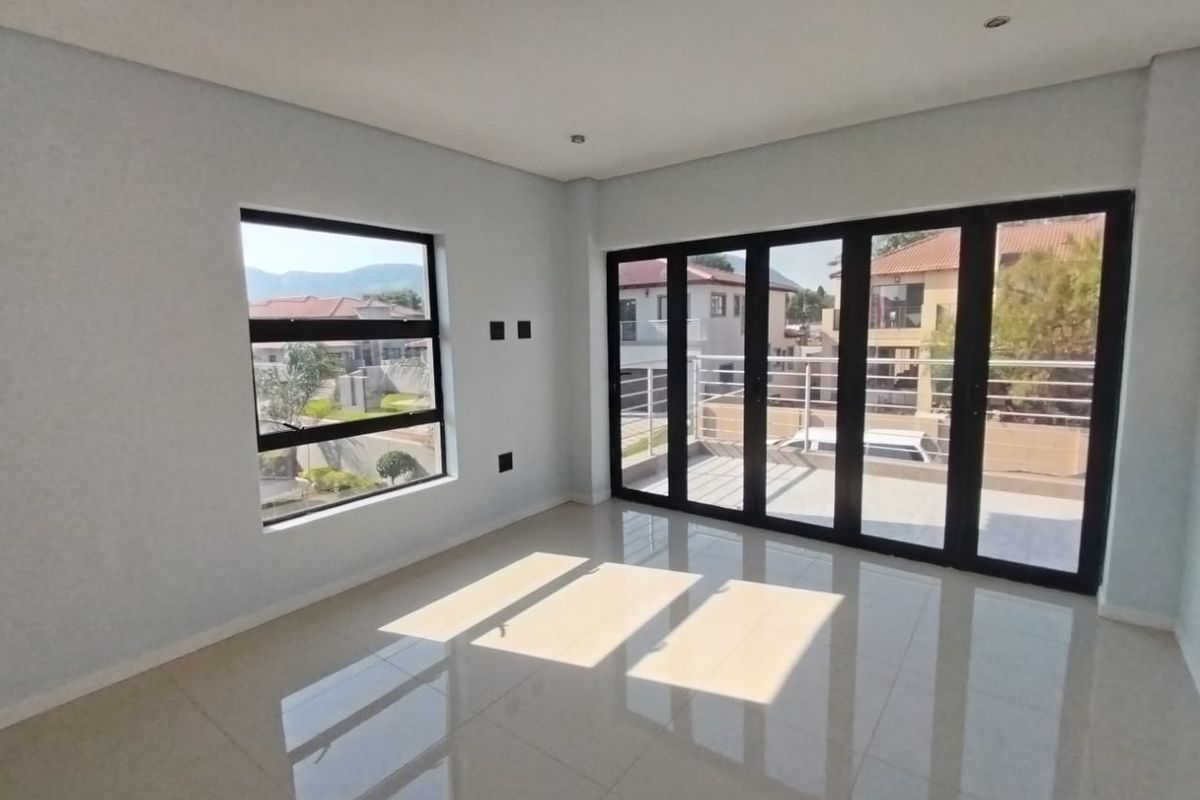 A bright, modern, and empty living area featuring large black aluminium folding doors leading to a balcony and tiled flooring throughout.