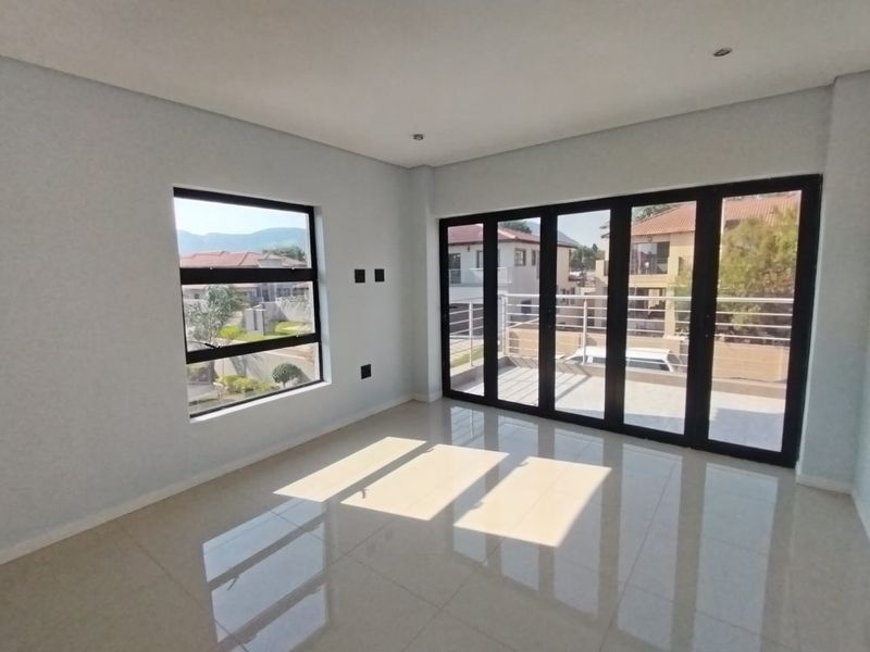 A bright, modern, and empty living area featuring large black aluminium folding doors leading to a balcony and tiled flooring throughout.