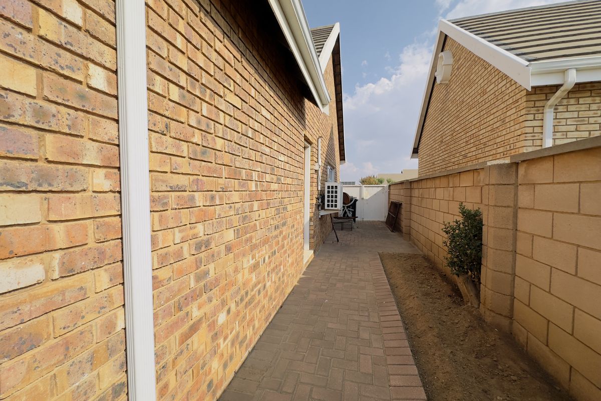 A side walkway featuring brick paving, face brick exterior walls, and a boundary wall, providing access between townhouse units.