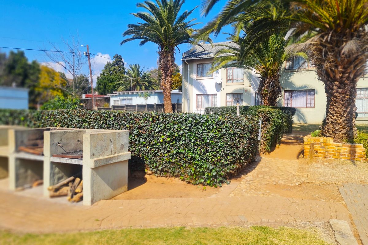 Outdoor communal area featuring a built-in concrete braai, paved pathways, and established palm trees set against the apartment building facade.