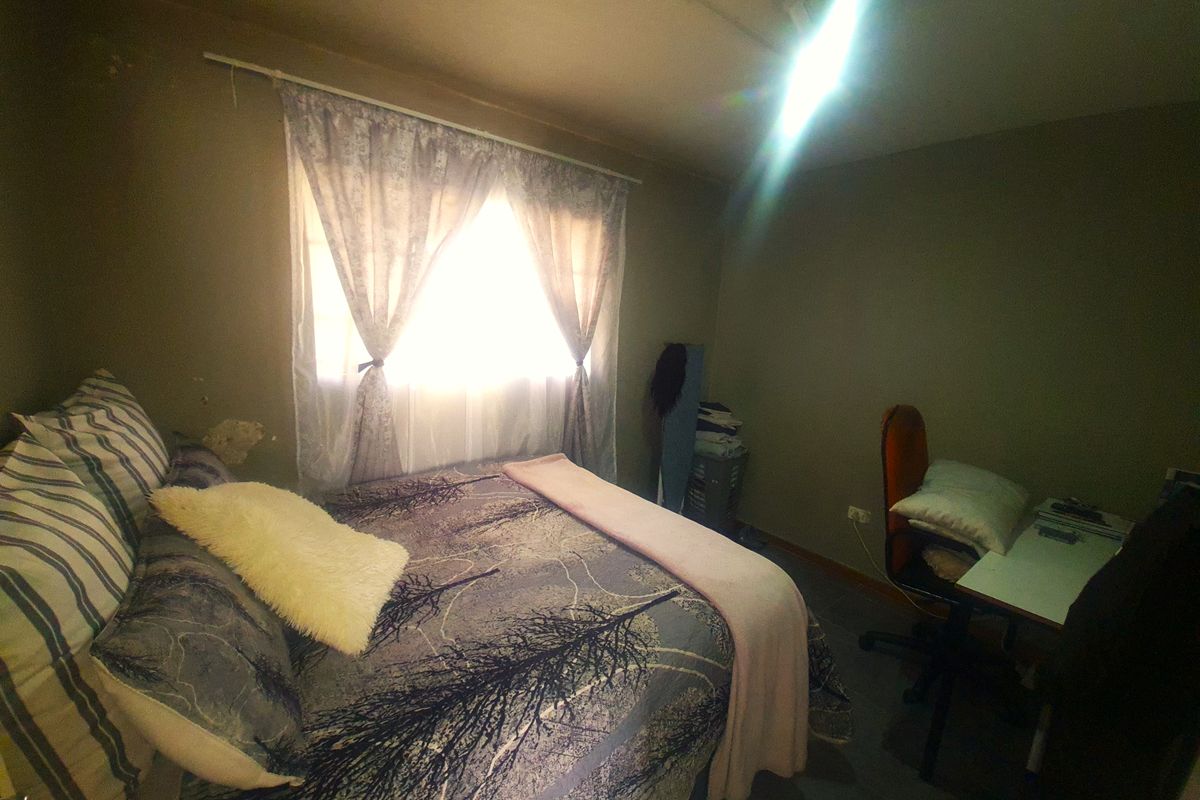 A bedroom featuring a window with curtains and visible wall surface wear, providing a functional space for rest or study.