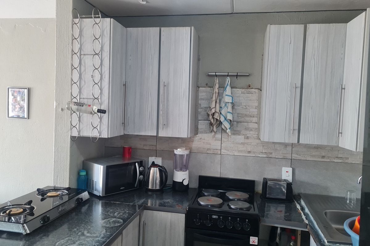 Compact kitchen featuring light wood-grain cabinetry, stone-look tile backsplash, and integrated stove and hob setup.
