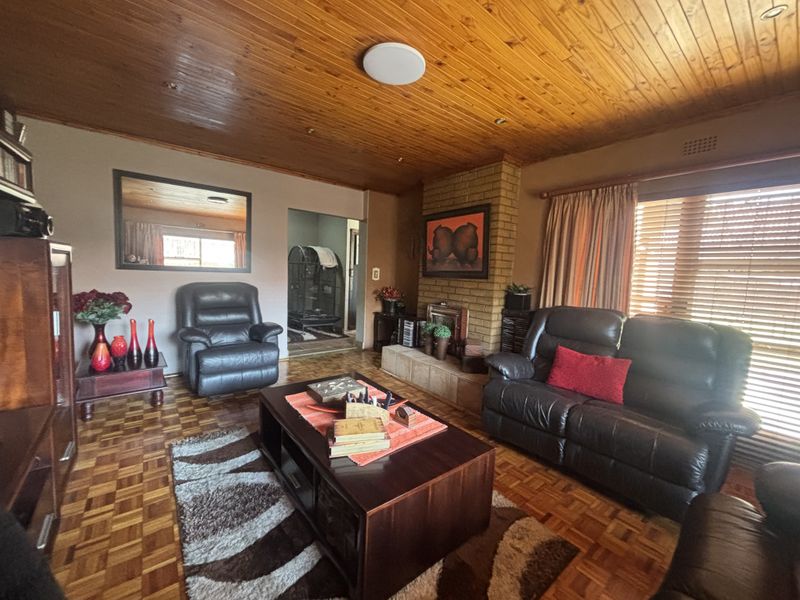 A cozy living room featuring a classic brick fireplace, warm timber tongue and groove ceiling, and traditional parquet flooring.