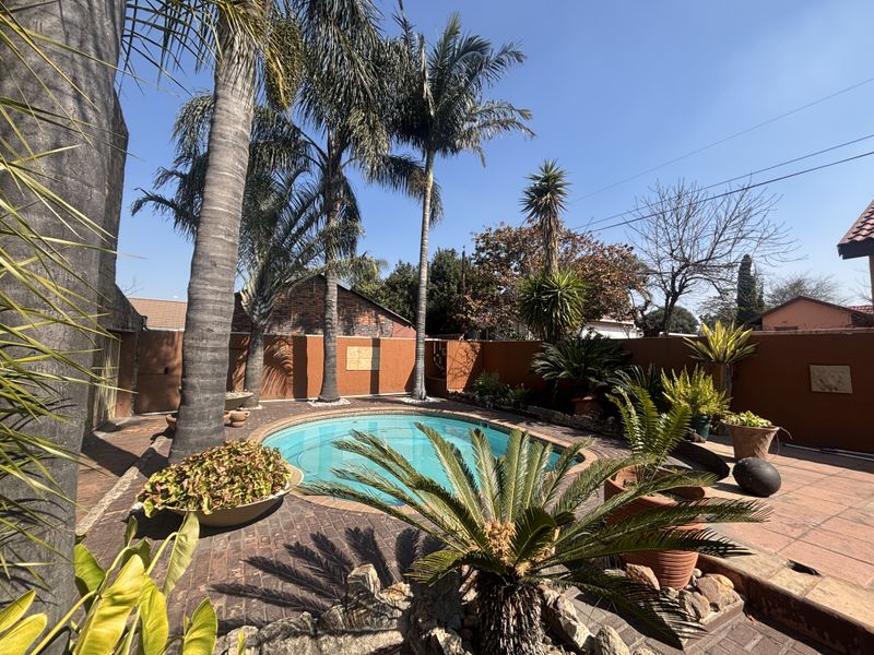 A private outdoor pool area featuring a circular swimming pool surrounded by brick paving and enclosed by a solid boundary wall.