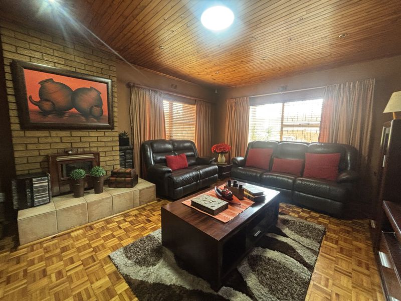 A cozy living room featuring a brick fireplace, warm wood-panelled ceilings, and classic parquet flooring, creating a traditional and inviting atmosphere.