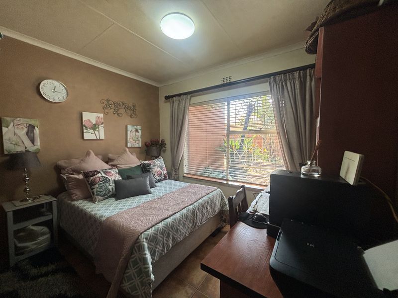 A functional bedroom featuring tiled flooring, a large window with blinds, and neutral wall tones, offering a comfortable and practical living space.