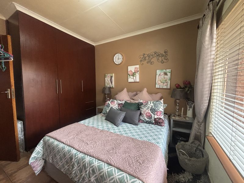 A cozy bedroom featuring dark wood built-in cupboards, tiled flooring, and venetian blinds, offering a functional and well-maintained living space.