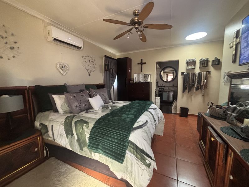 A spacious bedroom featuring tiled flooring, a ceiling fan, and a wall-mounted air conditioning unit, with direct access to an en-suite bathroom.
