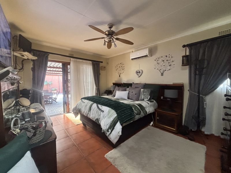 Spacious bedroom featuring tiled flooring, a ceiling fan, split-system air conditioning, and direct access to an outdoor patio area through sliding glass doors.