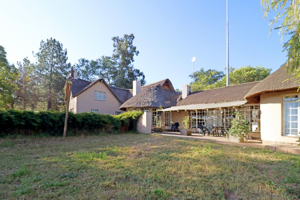 Rear view of a traditional thatched-roof house featuring a covered patio area and established garden surroundings.