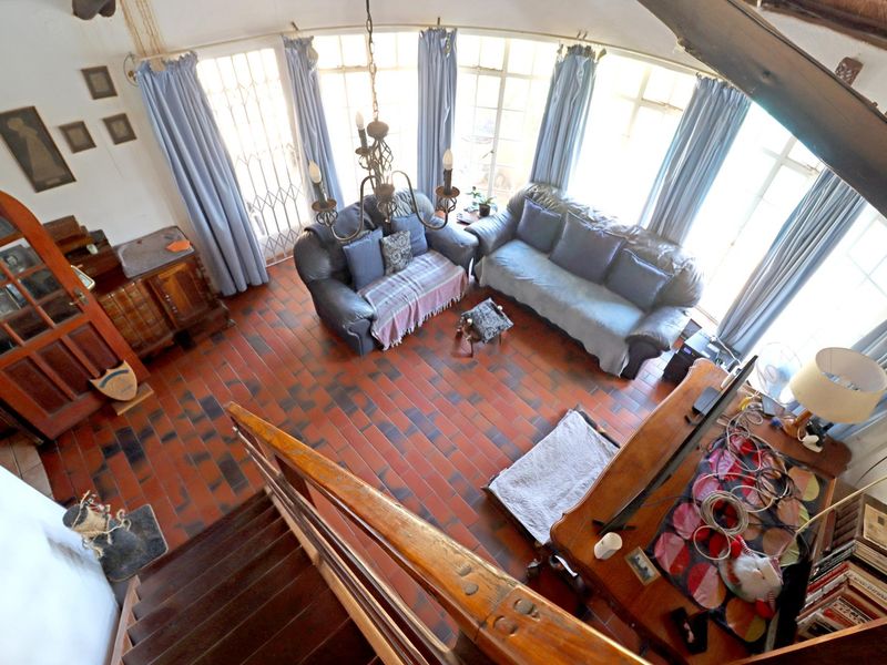 Spacious living room featuring terracotta tile flooring, a curved window wall with natural light, and a wooden staircase leading to the upper level.