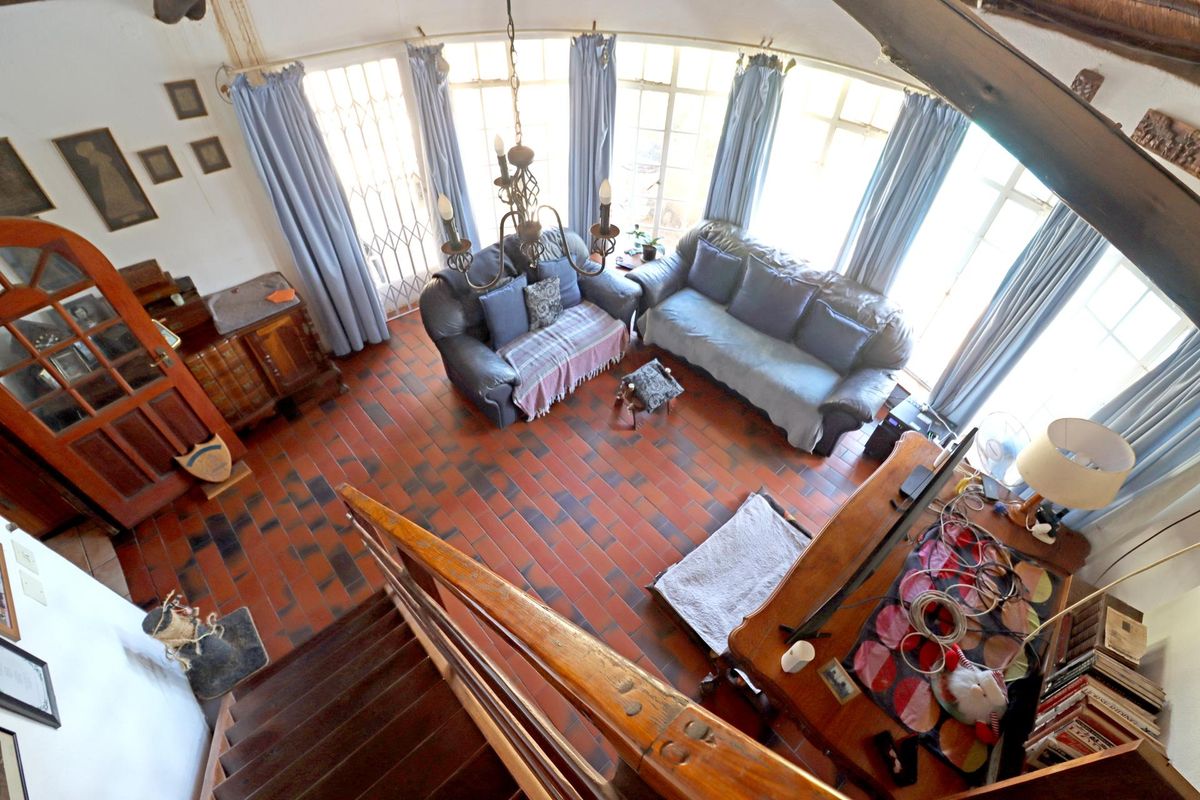 Spacious living room featuring terracotta tile flooring, a curved window wall with natural light, and a wooden staircase leading to the upper level.