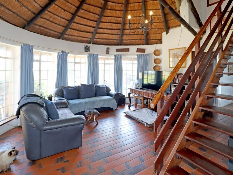 Spacious living area featuring a unique circular design with a traditional thatched roof, exposed timber rafters, and a wooden staircase.