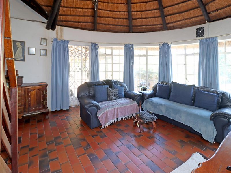 A circular living room featuring a traditional thatched roof with exposed timber rafters and terracotta tile flooring, offering a unique architectural aesthetic.