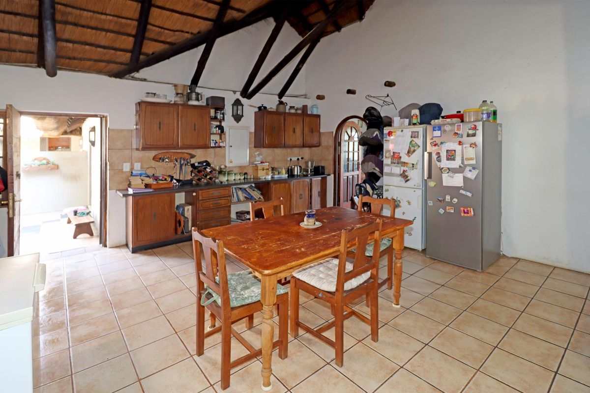 A rustic kitchen featuring exposed timber beams, a thatched ceiling, tiled flooring, and traditional wooden cabinetry, offering a warm, dated aesthetic.