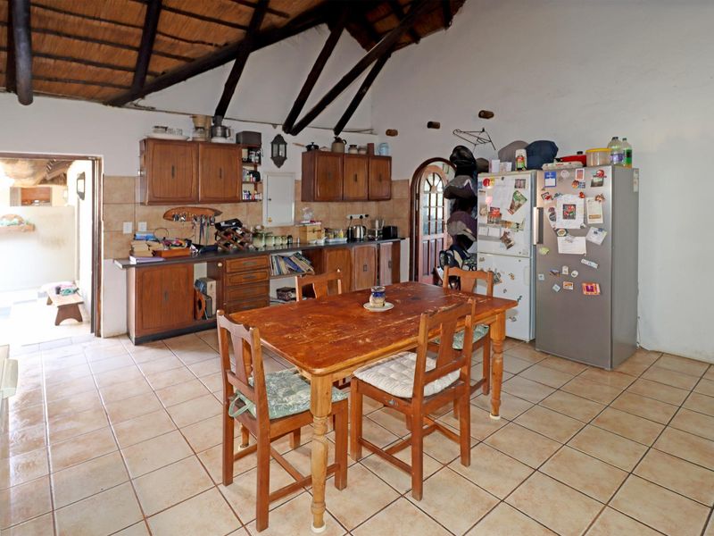 A rustic kitchen featuring exposed timber beams, a thatched ceiling, tiled flooring, and traditional wooden cabinetry, offering a warm, dated aesthetic.
