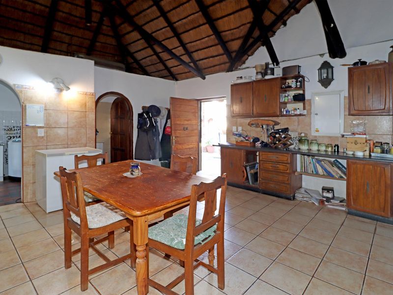 Open-plan kitchen and dining area featuring a high thatched ceiling with exposed timber beams, tiled flooring, and traditional wooden cabinetry.