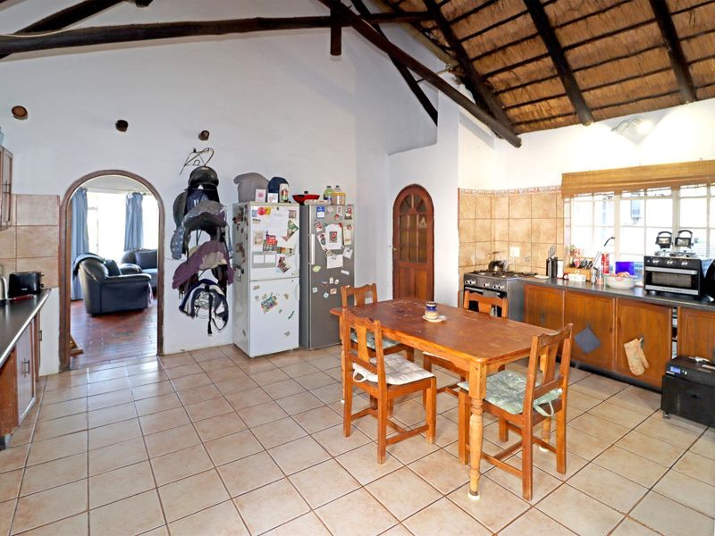 Open-plan kitchen and dining area featuring a high vaulted thatched ceiling with exposed timber rafters and tiled flooring throughout.