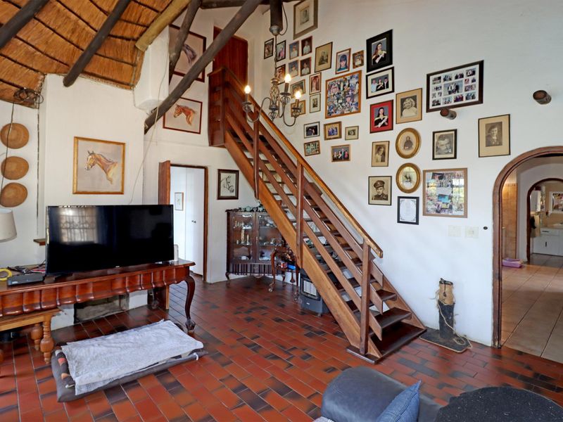 Spacious living area featuring a unique thatched ceiling with exposed timber rafters, a wooden staircase, and traditional terracotta tile flooring.