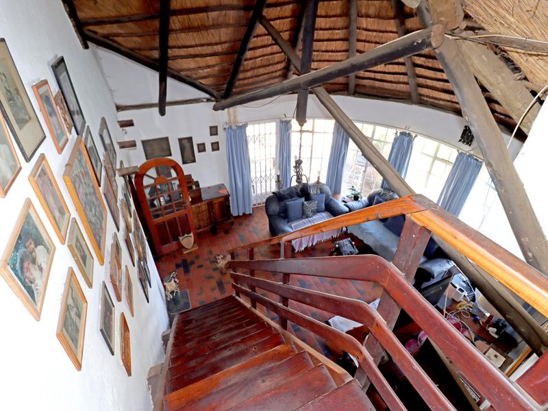A unique living area featuring a high thatched ceiling with exposed timber rafters, terracotta flooring, and a wooden staircase overlooking the space.