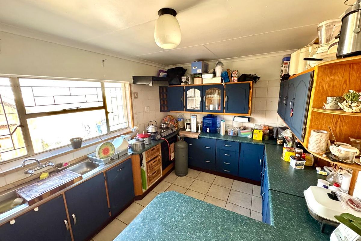 A functional kitchen featuring blue cabinetry, laminate countertops, a stainless steel sink, and large windows providing natural light.
