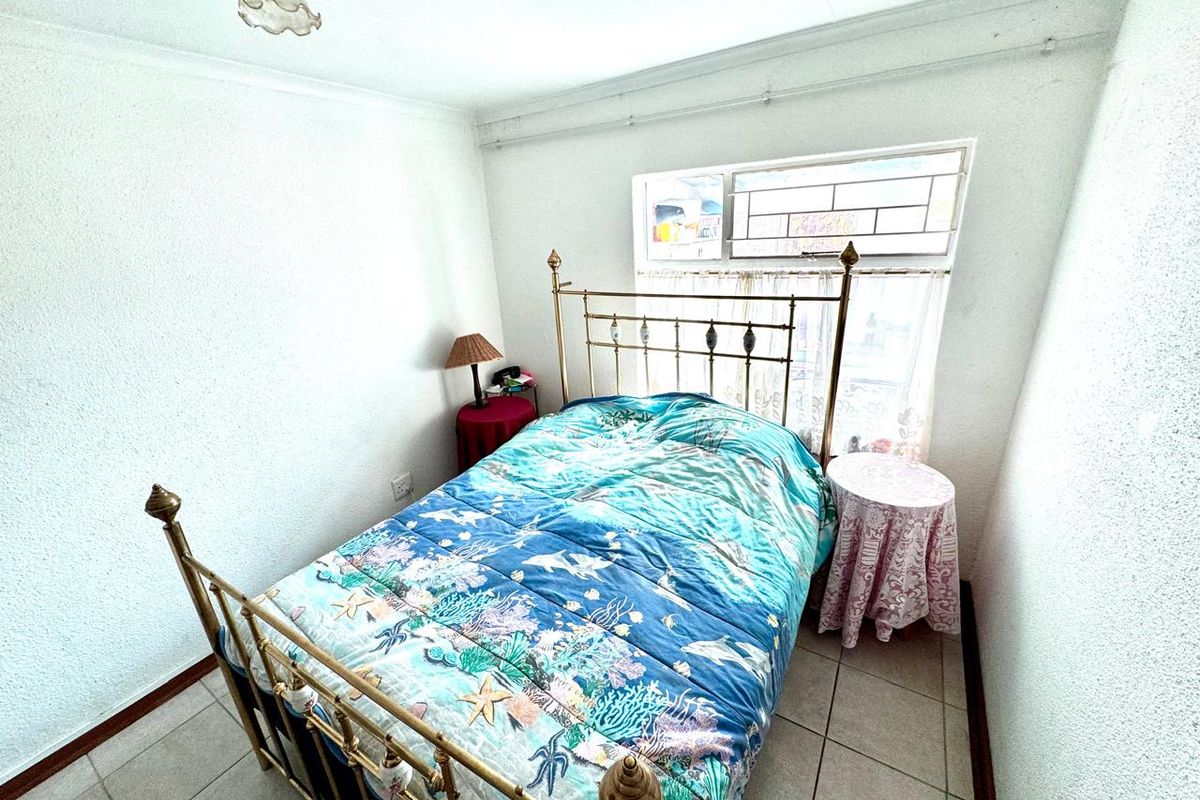A compact bedroom featuring tiled flooring, a window with security bars, and a simple ceiling light fixture.