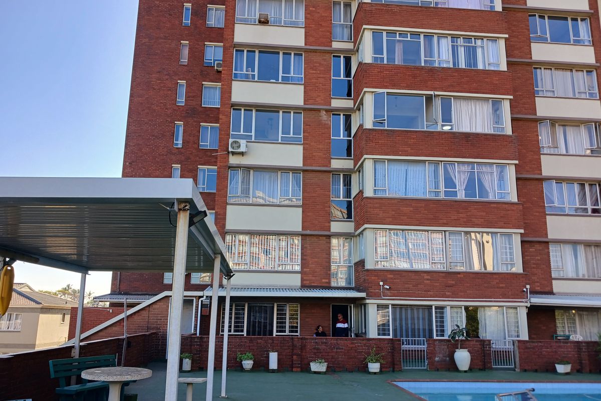 Exterior view of a multi-story brick apartment building featuring a communal swimming pool area and covered patio space.