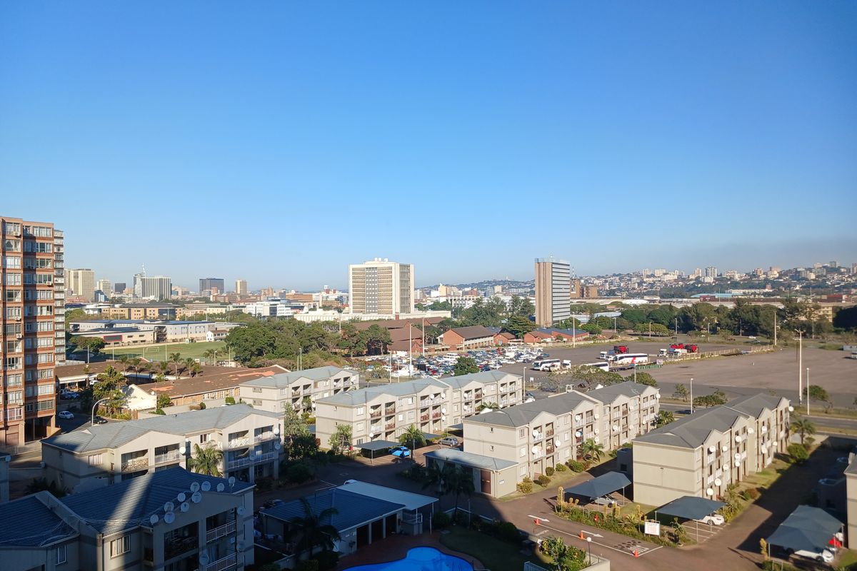 Elevated aerial view overlooking a residential apartment complex with a swimming pool and surrounding urban landscape.