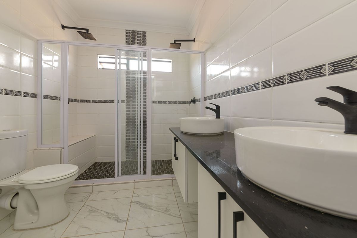 Modern bathroom featuring a double vanity with vessel sinks, black fixtures, and a spacious walk-in shower with decorative tile accents.