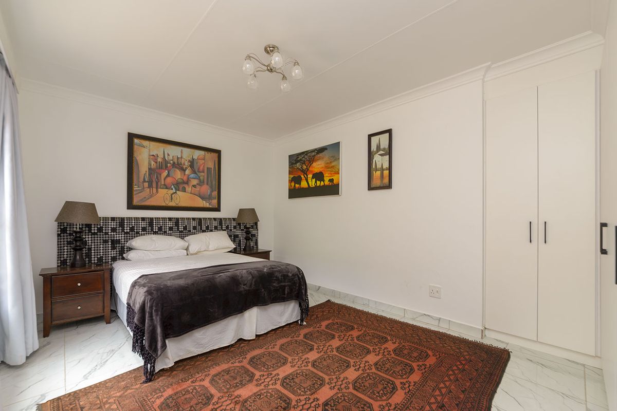 A well-maintained bedroom featuring built-in white cabinetry, marble-look tiled flooring, and crown molding, offering a clean and functional living space.