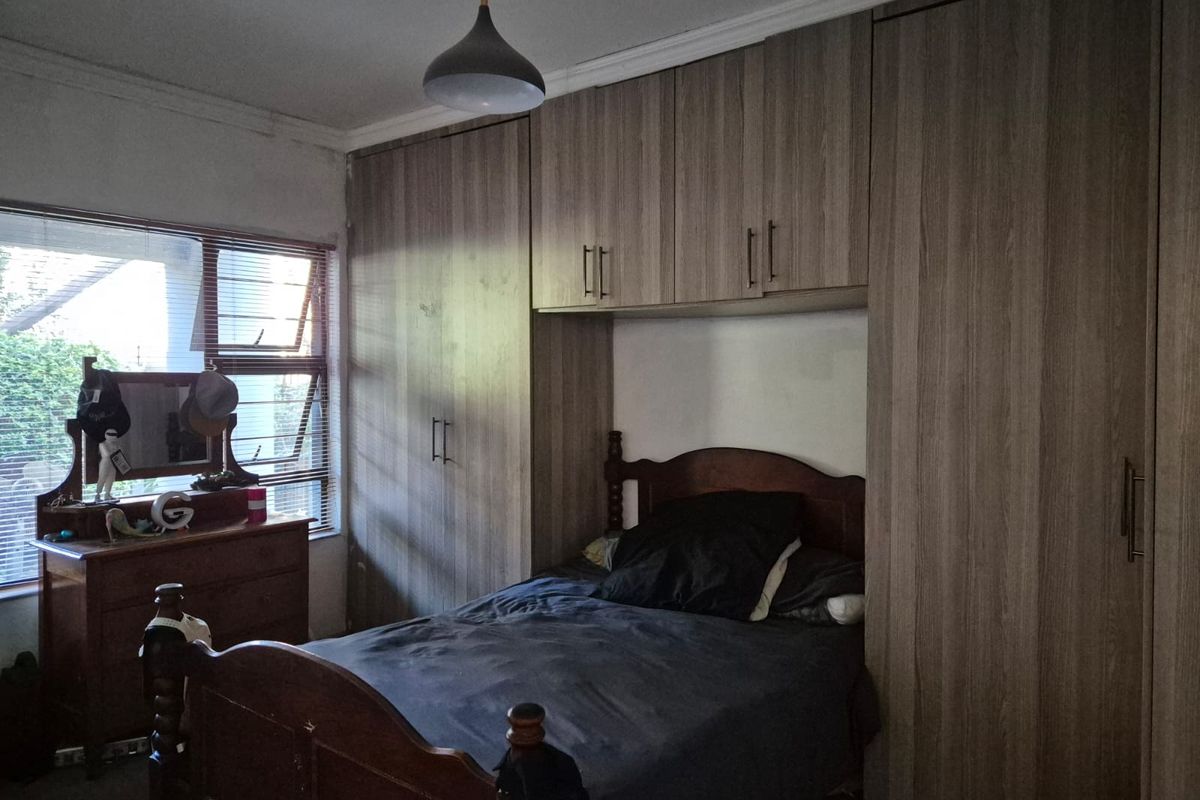 A bedroom featuring extensive built-in wooden cabinetry and a window with blinds, providing functional storage and natural light.