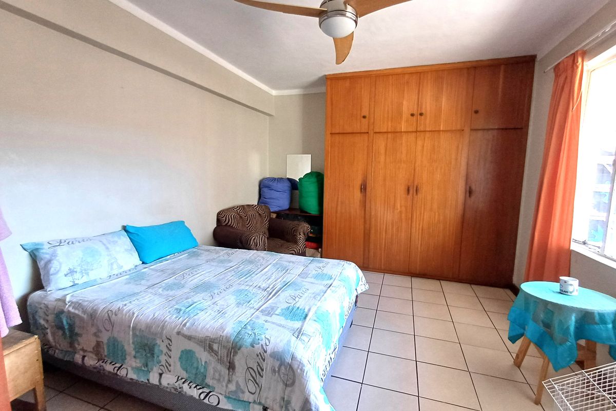 A bedroom featuring tiled flooring, a ceiling fan, and a large built-in wooden wardrobe providing ample storage space.