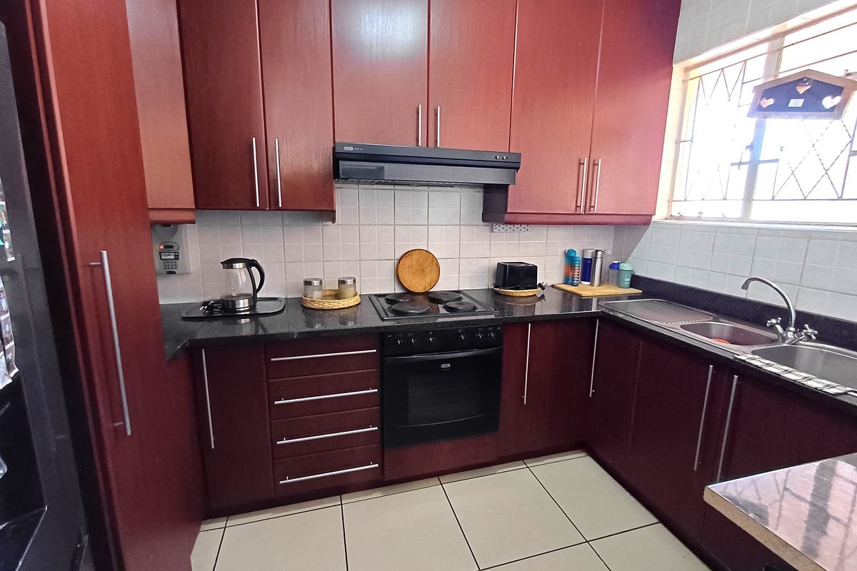 A functional kitchen featuring dark wood cabinetry, granite countertops, built-in oven, electric hob, extractor fan, and a stainless steel sink with tiled finishes.