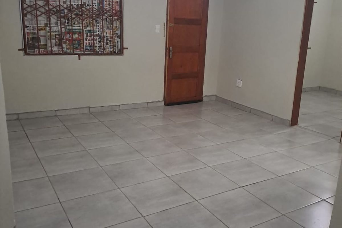 An empty living room featuring tiled flooring, a wooden door, and a decorative ceiling feature with security bars on the window.