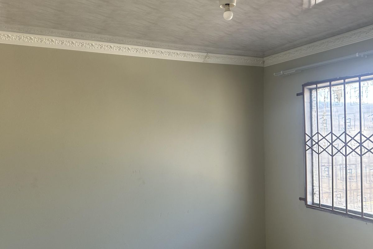 An empty bedroom featuring tiled flooring, decorative cornice, and a security gate on the window, currently undergoing minor renovations.