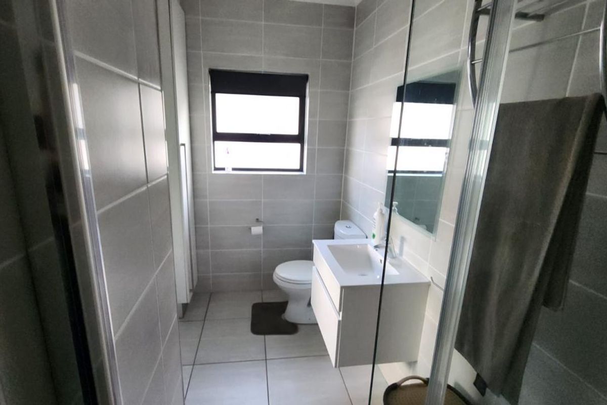 Modern bathroom featuring a wall-mounted vanity, glass shower enclosure, and neutral ceramic tiling throughout.