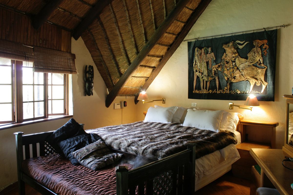 Cozy bedroom featuring a traditional thatched roof with exposed timber beams, warm lighting, and a window with wooden blinds.