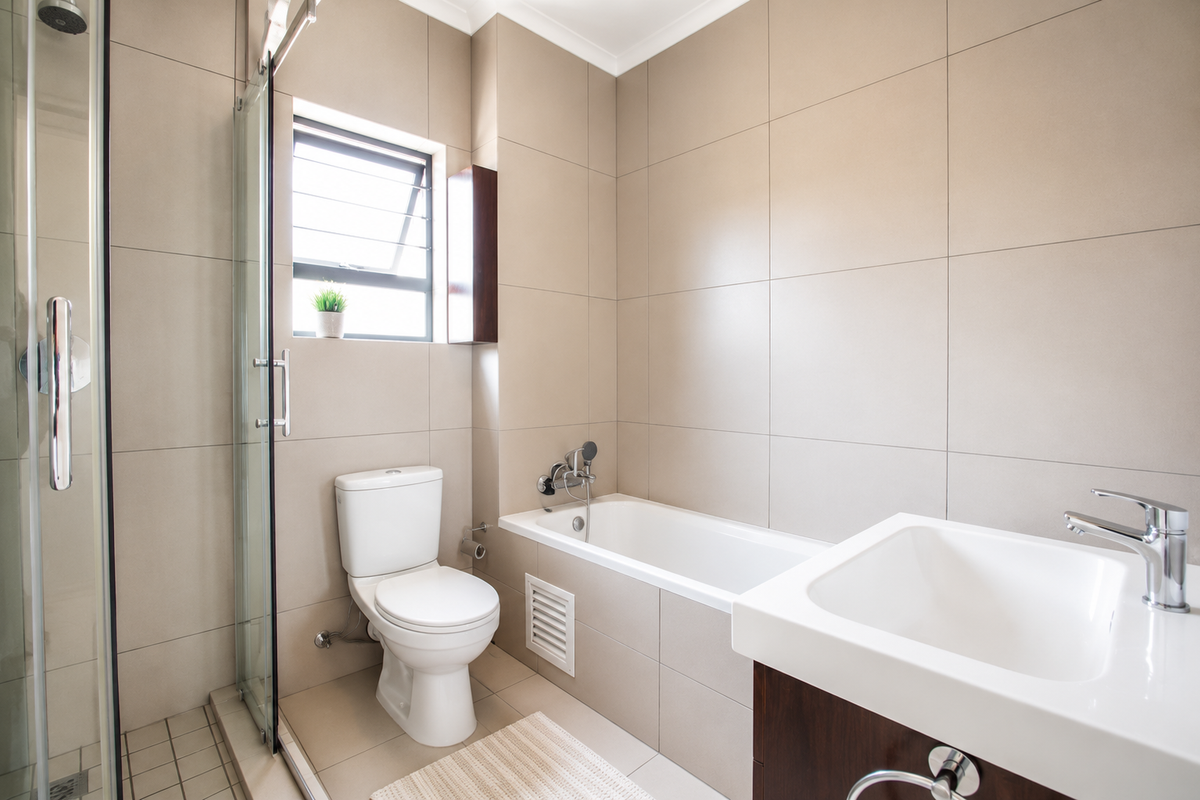 Modern bathroom featuring a glass-enclosed shower, built-in bathtub, vanity basin, and neutral floor-to-ceiling wall tiles.