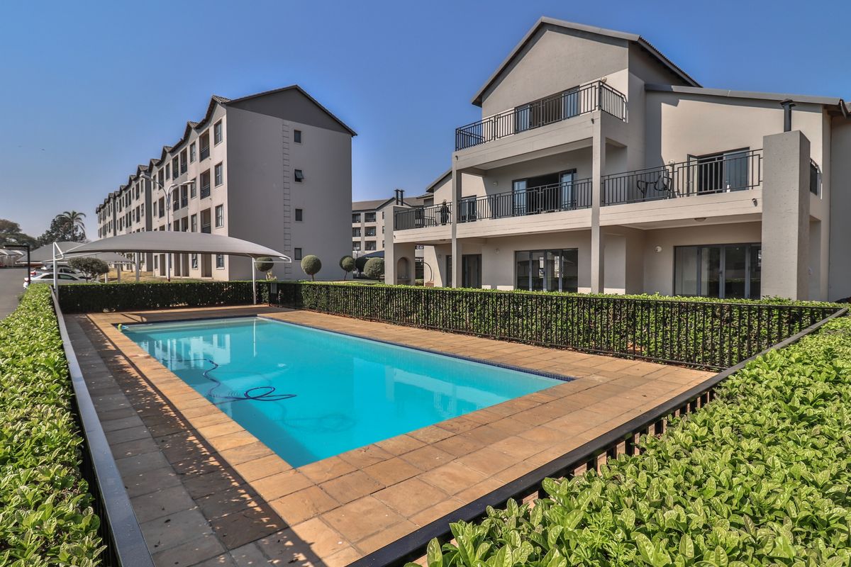 A well-maintained communal swimming pool area featuring paved decking, metal safety fencing, and views of the apartment complex buildings.