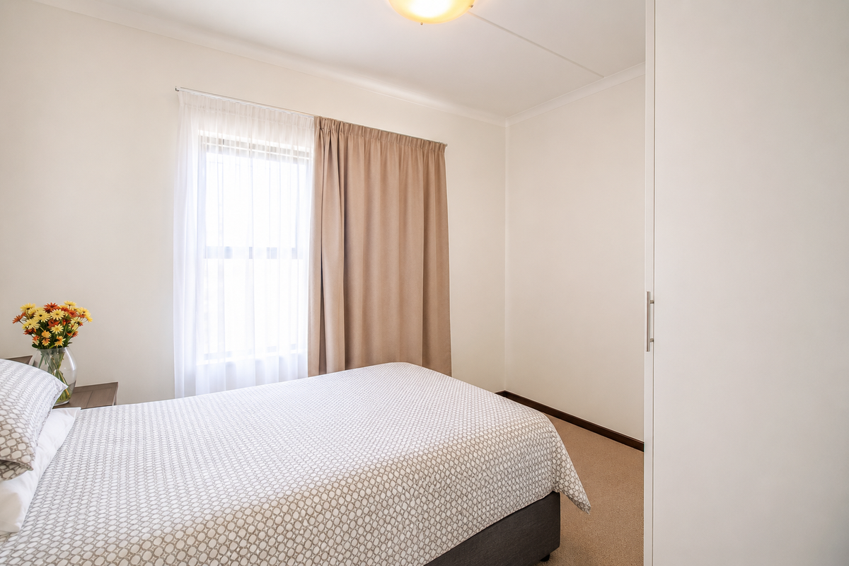 A clean and well-maintained bedroom featuring neutral walls, carpeted flooring, and a built-in wardrobe, offering a bright and comfortable living space.