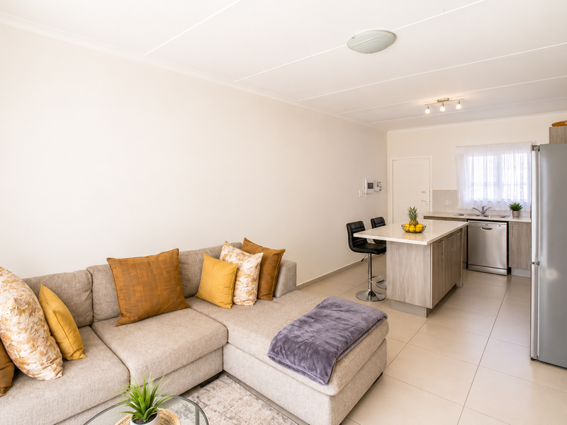 Open-plan living area featuring a modern kitchen with island, stainless steel dishwasher, and tiled flooring throughout the combined space.