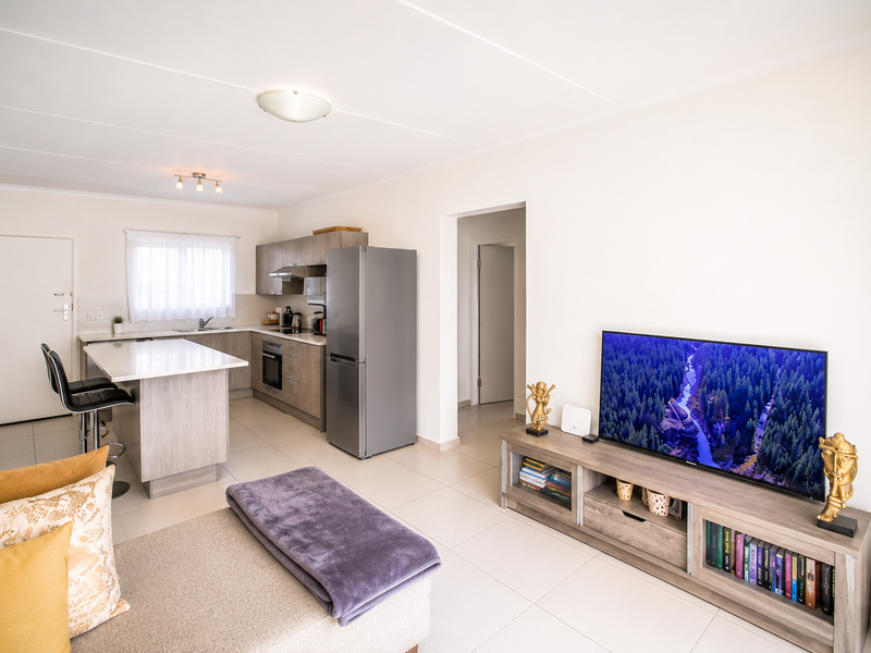 A bright open-plan living and kitchen area featuring modern wood-finish cabinetry, a central kitchen island, and neutral tiled flooring throughout.