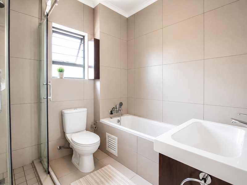 Modern bathroom featuring a glass-enclosed shower, built-in bathtub, vanity basin, and neutral floor-to-ceiling wall tiles.